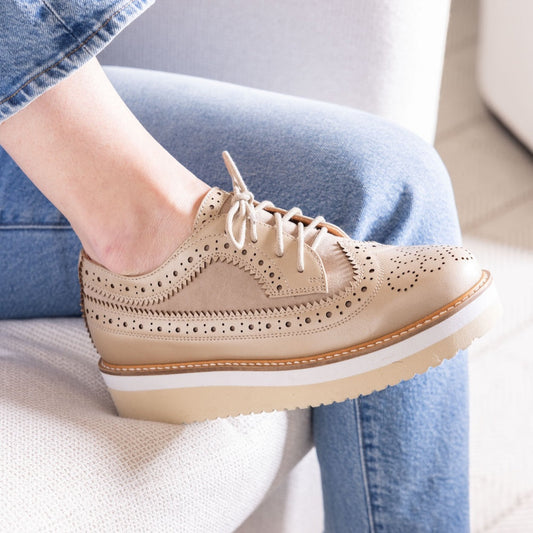 Beige brogue shoes worn with blue jeans on a light background