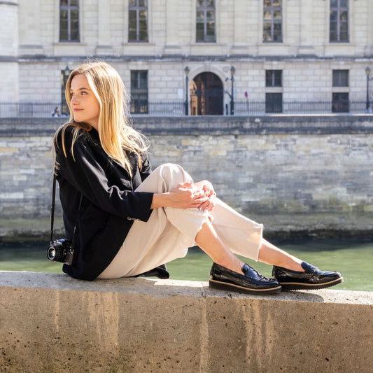 Woman sitting on a stone ledge by a canal with a classical building in the background
