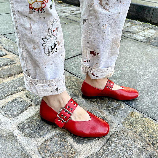 Red shoes worn with white pants featuring cartoon designs on a stone pavement.