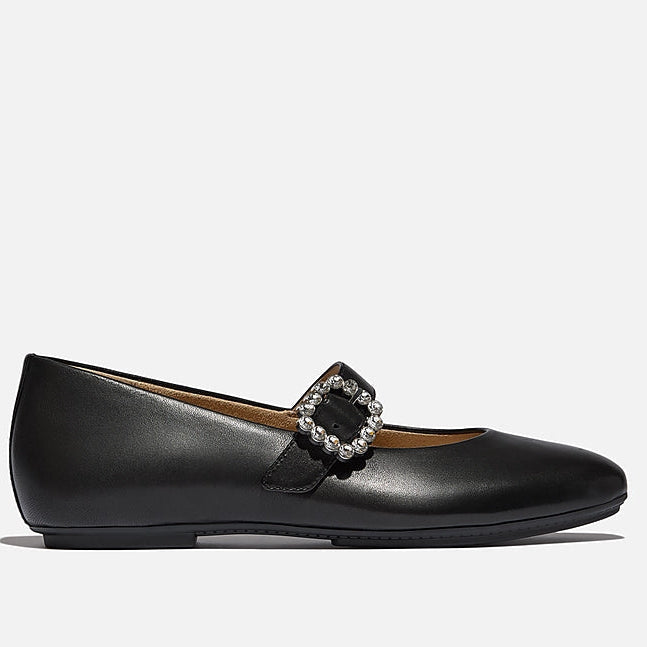 Black flat shoe with a decorative buckle on a light gray background